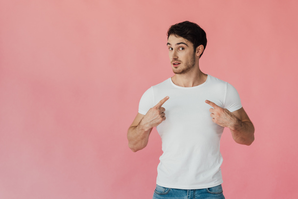 muskularny Człowiek w białym t-shirt wskazujący palce na siebie izolowane na różowym - Zdjęcie, obraz