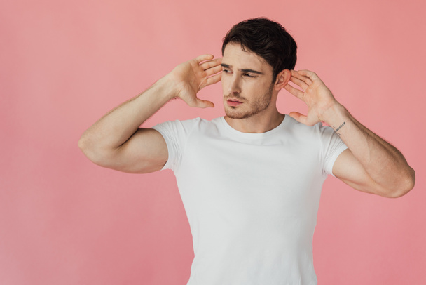 muscular man in white t-shirt holding palms near ears and listening isolated on pink - Foto, Bild