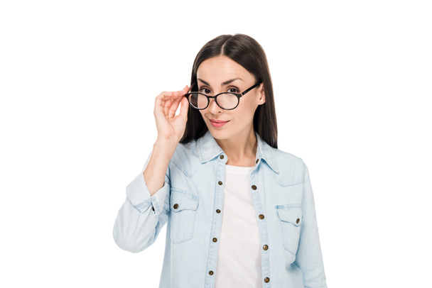 podivná brunetka v brýlích a džíšových bundě s pohledem na kameru izolovanou na bílém - Fotografie, Obrázek