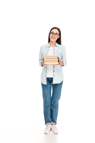 счастливая брюнетка девушка в очках в джинсовой куртке с книгами изолированы на белом
 - Фото, изображение