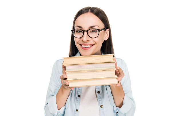 happy brunette girl in glasses in denim jacket holding books isolated on white - Фото, изображение