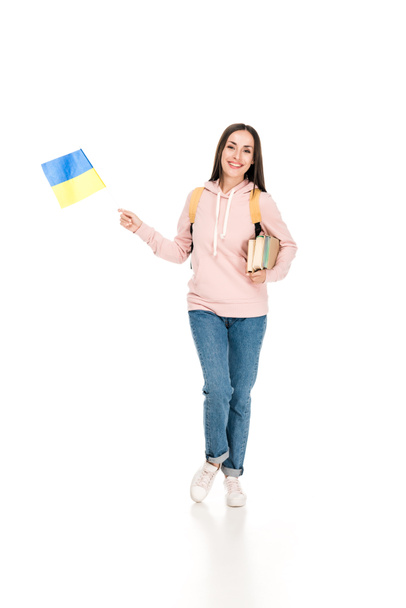 Plná délka pohled na usmívajícího se studenta s batohu, který drží ukrajinskou vlajku a knihy izolované na bílém - Fotografie, Obrázek