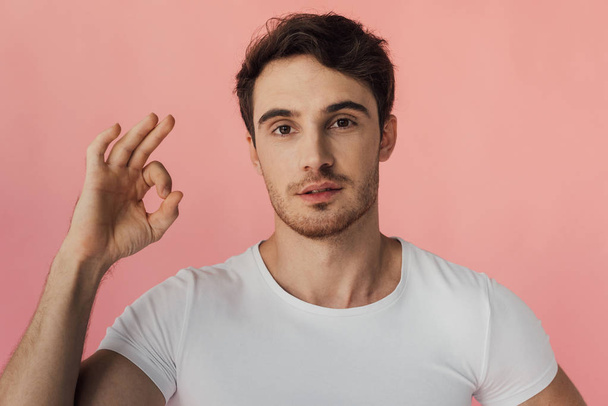 front view of muscular man in white t-shirt showing okay sign isolated on pink - Foto, afbeelding