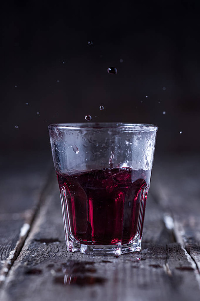 Shot of Red Bitter Liquor with Drops Splashing on Wood - Photo, Image