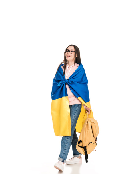 vista completa de la joven feliz en gafas caminando con la mochila y la bandera de Ucrania en los hombros aislados en blanco
 - Foto, Imagen