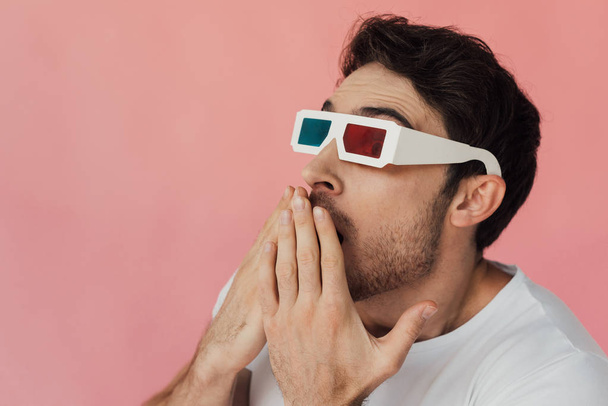 geschokt gespierde man in 3D bril bedekt mond met handen geïsoleerd op roze - Foto, afbeelding
