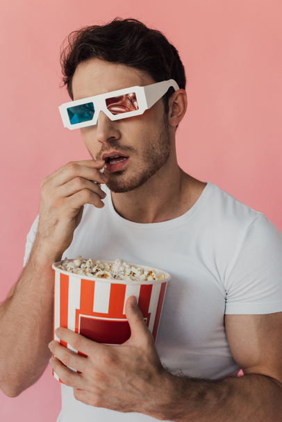 περίεργος μυώδης άνθρωπος σε 3D γυαλιά τρώγοντας ποπ κορν απομονωθεί σε ροζ - Φωτογραφία, εικόνα