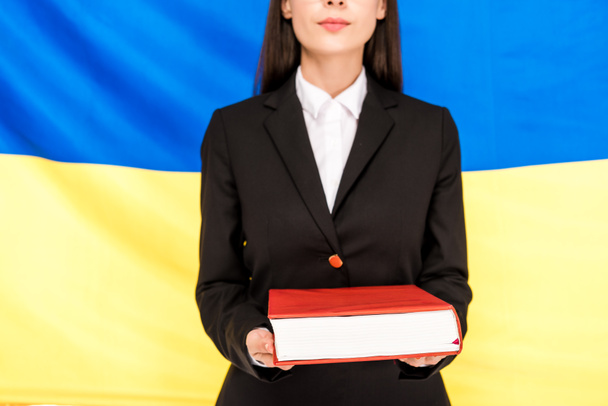 cropped view of lawyer in black suit holding book on Ukrainian flag background - Photo, Image