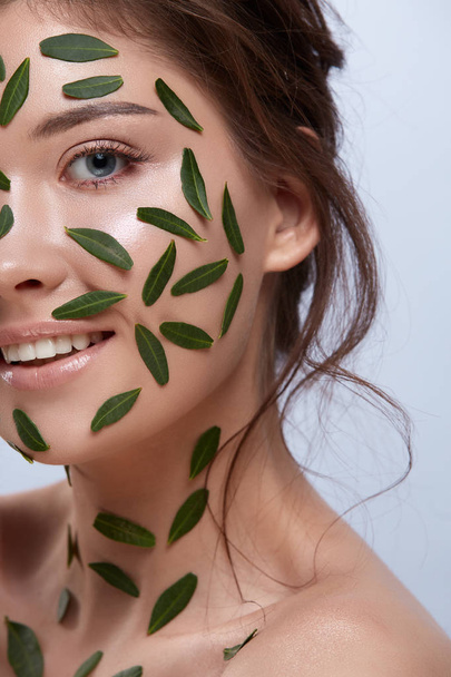 atractiva mujer con hojas verdes en la cara sobre fondo gris
 - Foto, Imagen