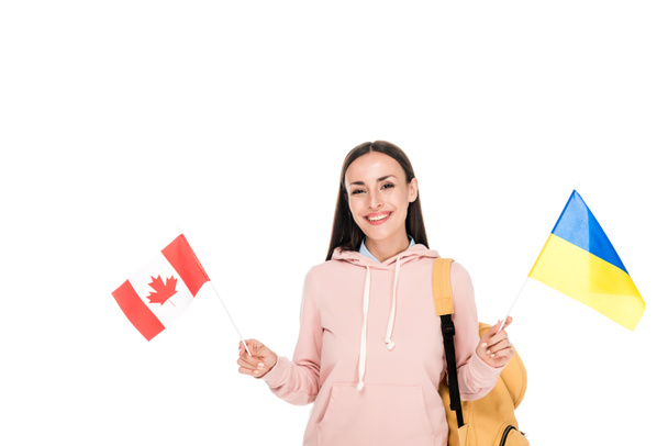 lachende student met rugzak die Oekraïense en Canadese vlaggen geïsoleerd op wit - Foto, afbeelding