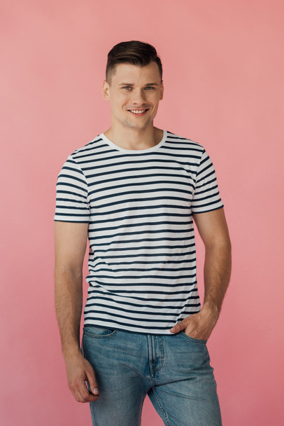 smiling man in striped t-shirt with hand in pocket looking at camera isolated on pink - Fotó, kép