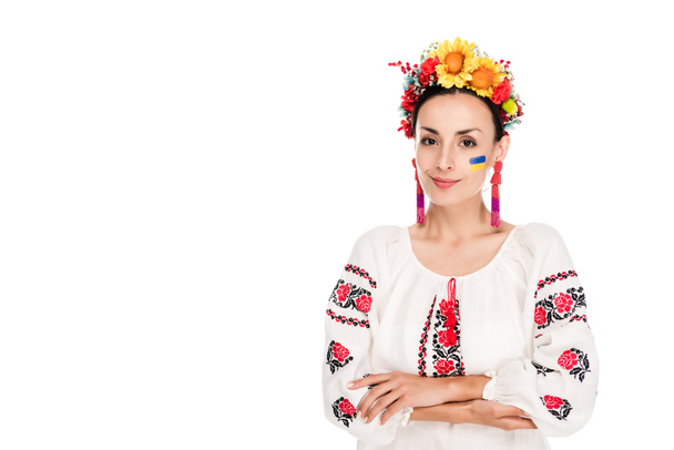 brünette junge Frau im nationalen ukrainischen bestickten Hemd und Blumenkranz mit verschränkten Armen auf weißem Grund - Foto, Bild