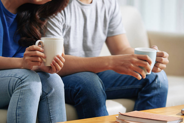 Couple sitting on sofa with tea or coffee cups  - Фото, зображення
