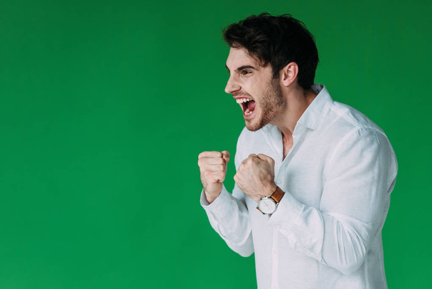 homem com raiva na camisa branca segurando punhos para cima e gritando isolado no verde
 - Foto, Imagem