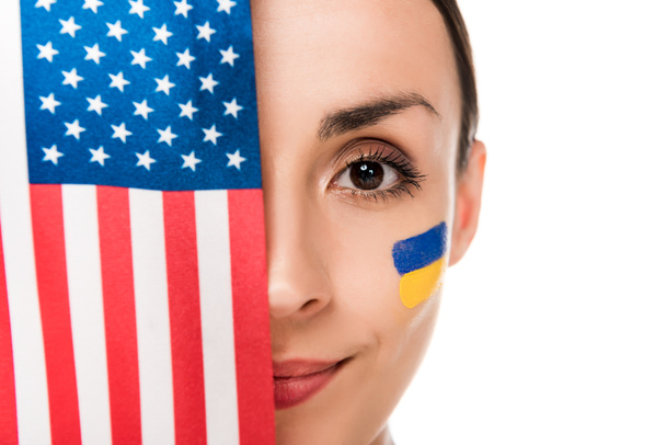 smiling young woman with painted Ukrainian flag on face holding American flag isolated on white - Фото, зображення