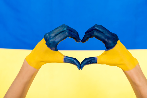 cropped view of painted hands showing heart sign on Ukrainian flag background - Foto, Imagem