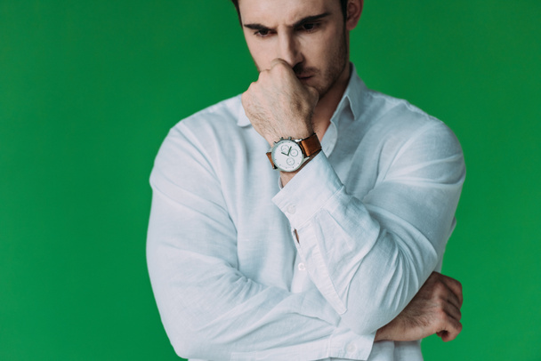 cropped view of serious pensive man in white shirt and wristwatch touching face with hand isolated on green - Foto, Imagem