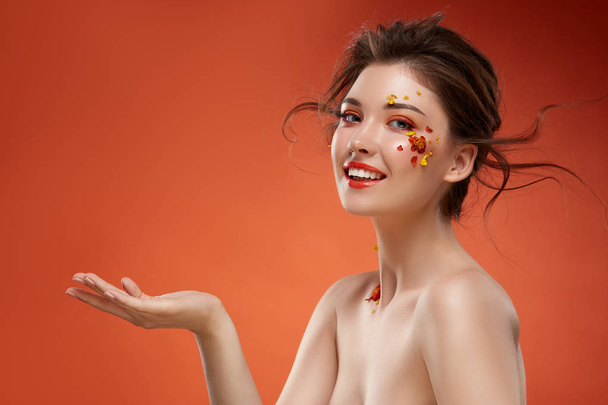 portrait of attractive woman with flowers on face on orange backdrop - Photo, Image