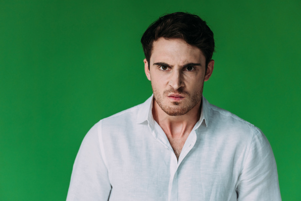 vista frontal del hombre enojado en camisa blanca mirando a la cámara aislada en verde
 - Foto, Imagen