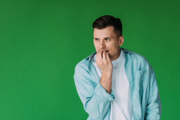 worried young man in shirt biting fingers and looking away isolated on green - Fotografie, Obrázek