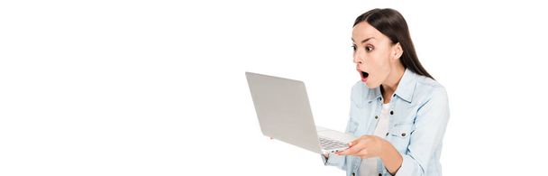 Schockiertes Mädchen in Jeansjacke mit Laptop auf weißer, panoramischer Aufnahme - Foto, Bild