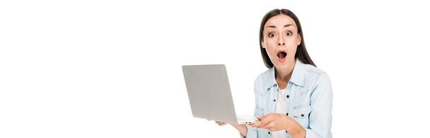 šokovaná dívka v džínové bundě s laptopem izolovaně na bílém, panoramatickém záběru - Fotografie, Obrázek