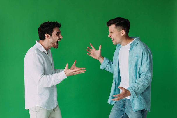 two men in shirts quarreling and screaming at each other isolated on green - Photo, Image