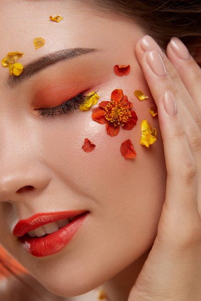 Porträt einer attraktiven Frau mit Blumen im Gesicht auf orangefarbenem Hintergrund - Foto, Bild