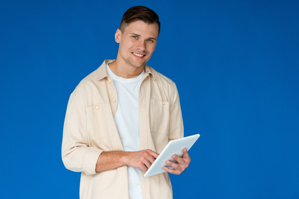 smiling young man in shirt using digital tablet isolated on blue - Фото, изображение