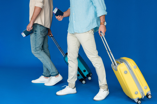 vista cortada de dois turistas segurando malas e passaportes com passagens aéreas em azul
 - Foto, Imagem