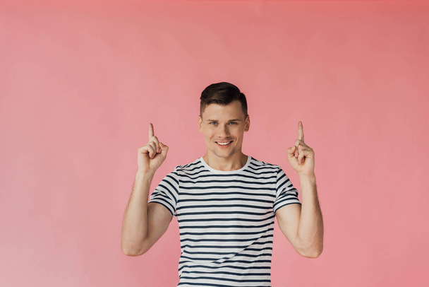 front view of smiling young man in striped t-shirt showing idea signs isolated on pink - Fotoğraf, Görsel