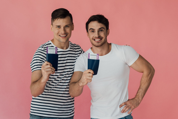 Vooraanzicht van twee opgewonden toeristen glimlachen en het houden van paspoorten met vliegtickets geïsoleerd op roze - Foto, afbeelding