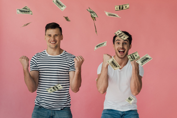 вид спереди двух возбужденных друзей с долларовыми банкнотами, показывающими да жестами, изолированными на розовом фоне
 - Фото, изображение