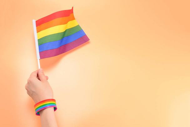 ЛГБТ-флаг в руке женщины на оранжевом фоне. Копирование пространства
.  - Фото, изображение
