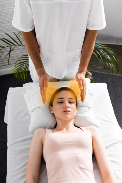 woman lying on massage table with closed eyes while healer cleaning her aura - Photo, Image