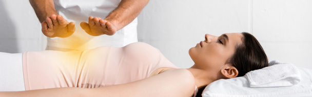 panoramische foto van genezer staande in de buurt van de vrouw en het vasthouden van de handen boven haar maag - Foto, afbeelding