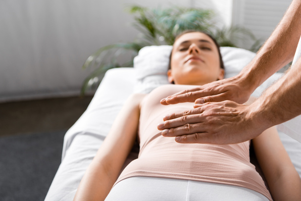 bijgesneden weergave van genezer staande in de buurt van vrouw en het vasthouden van handen boven haar maag - Foto, afbeelding