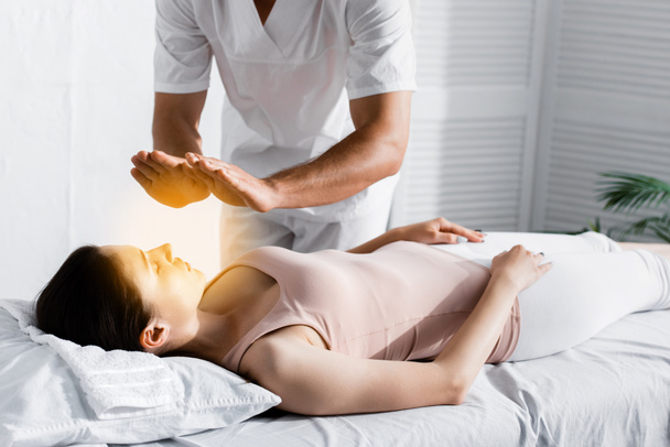 vista recortada del sanador de pie cerca de la mujer en la mesa de masaje y la limpieza de su aura
 - Foto, imagen