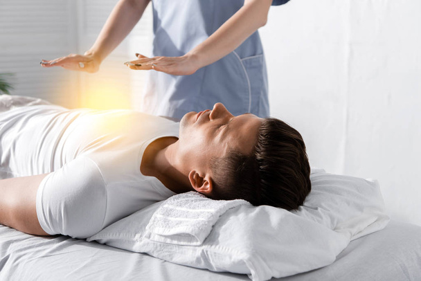 visão parcial do curandeiro em pé perto do homem na mesa de massagem e segurando as mãos acima de seu corpo
 - Foto, Imagem