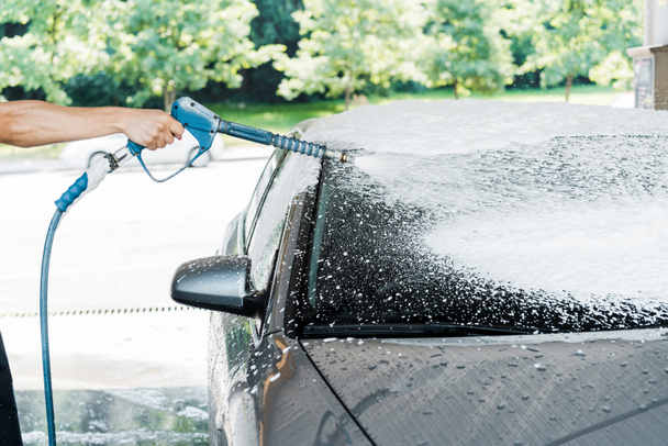 περικομμένη όψη του πλυντηρίου αυτοκινήτων που κρατά το πλυντήριο με αφρό κοντά στο αυτοκίνητο  - Φωτογραφία, εικόνα