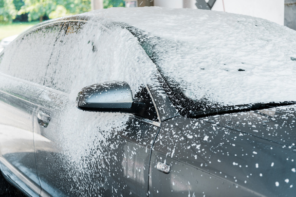 moderní šedé auto s bílou pěnou ve mytí aut  - Fotografie, Obrázek