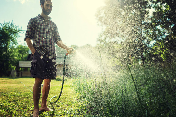 Hipster young man watering plants in a country house, summer and - Fotografie, Obrázek
