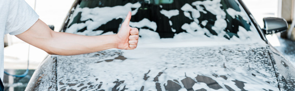 panoramic shot of car cleaner showing thumb up near car with foam  - Fotoğraf, Görsel