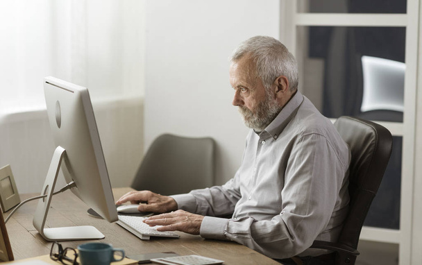 Senior man using his computer at home - Fotó, kép