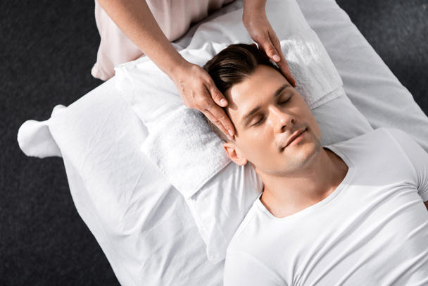 обрезанный вид массажера, стоящего рядом с человеком с закрытыми глазами и трогающего его лицо
 - Фото, изображение