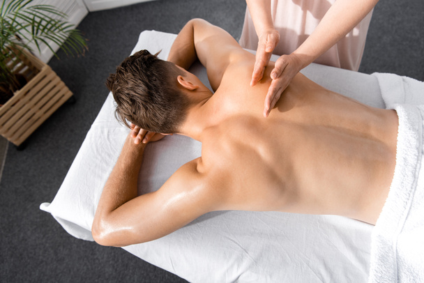 vista cortada de massagista e homem sem camisa deitado na mesa de massagem
 - Foto, Imagem