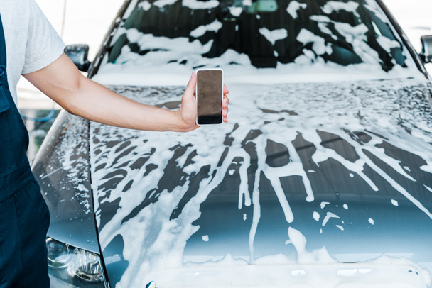 vue recadrée de l'homme tenant smartphone avec écran blanc près de la voiture avec de la mousse
  - Photo, image