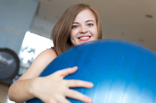 Spor salonunda mavi jimnastik topu üzerinde gülümseyen genç beyaz kadın kız, egzersiz veya yoga pilates egzersiz yapıyor - Fotoğraf, Görsel