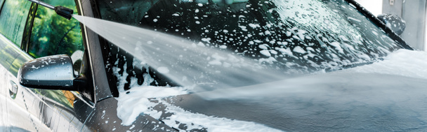 panoramic shot of pressure washer with water on grey modern car with foam  - Фото, изображение