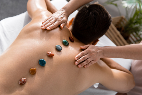 cropped view of masseur and shirtless man with stones on back - Foto, Bild
